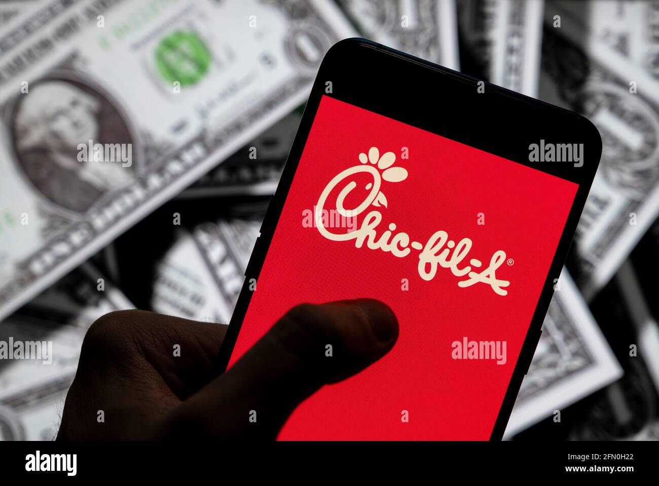 In this photo illustration the American fast food restaurant chain Chick-fil-A logo seen displayed on a smartphone with USD (United States dollar) currency in the background. Stock Photo