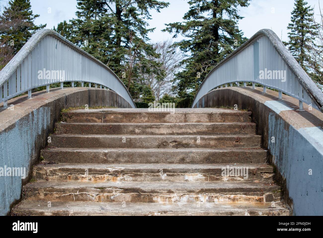 The narrow stairway to an old cantilever style footbridge. The cement bridge is worn and textured. Stock Photo