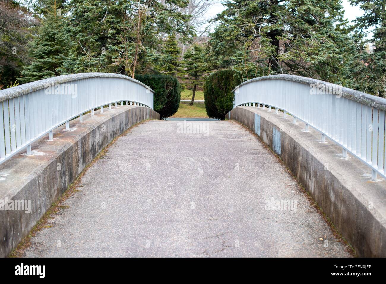 A vintage concrete pathway cantilever bridge spanning over a path in a park. Stock Photo