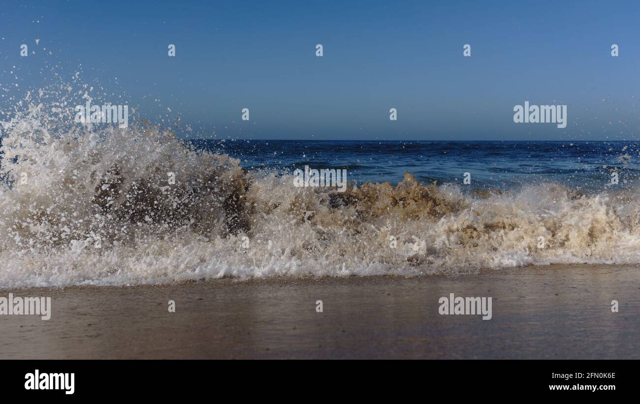 Ocean wave crushing onto sandy beach on a sunny day in Southern ...
