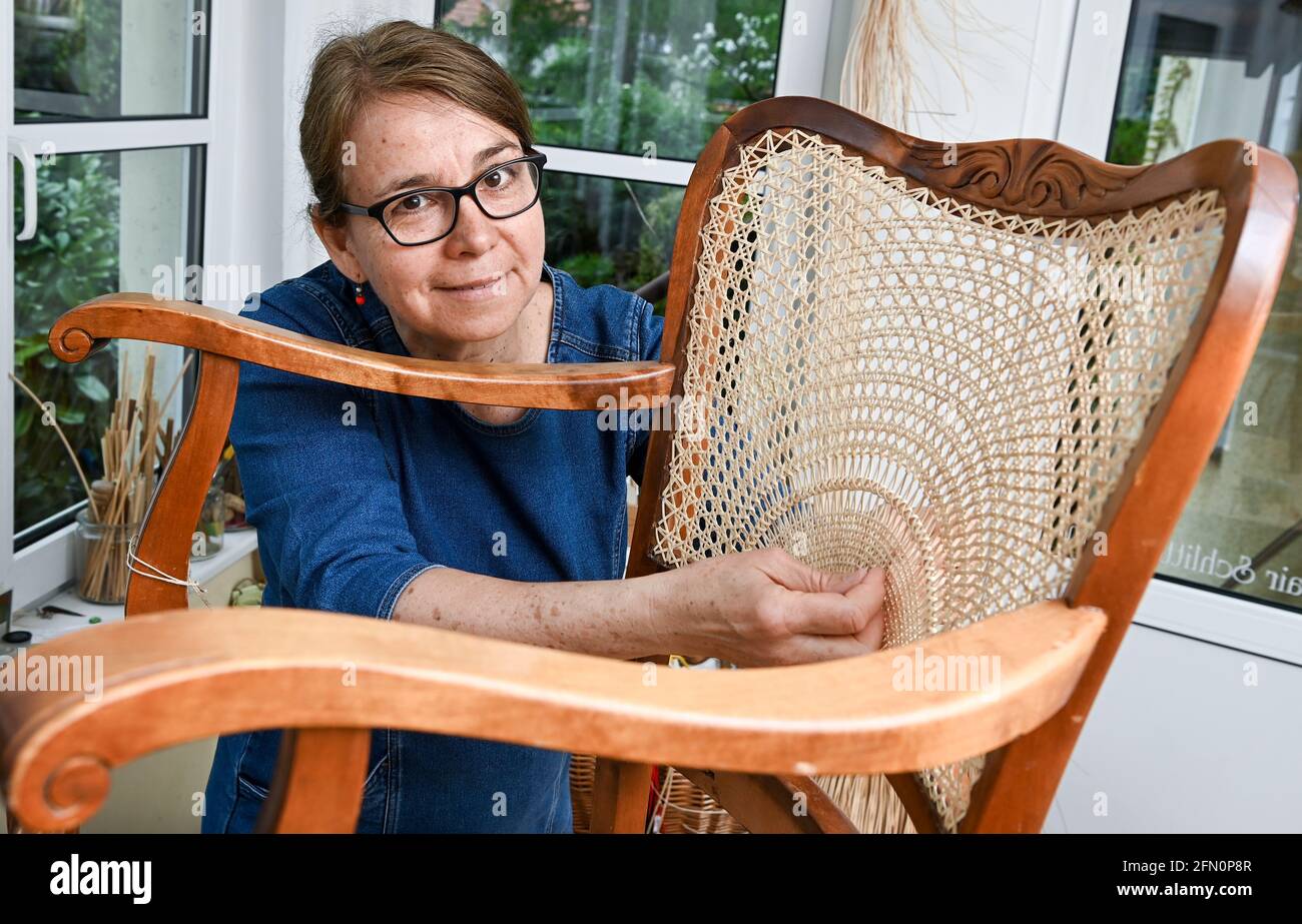 Berlin, Germany. 12th May, 2021. Chair weaver Silke Schlittermann works on  repairing an armchair with half sun weave in her workshop in Köpenick.  Chair weaving cane, the bark of rattan, is used