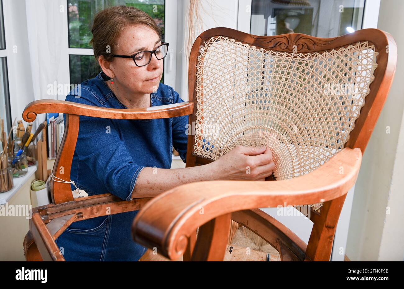 Berlin, Germany. 12th May, 2021. Chair weaver Silke Schlittermann works on  repairing an armchair with half sun weave in her workshop in Köpenick.  Chair weaving cane, the bark of rattan, is used