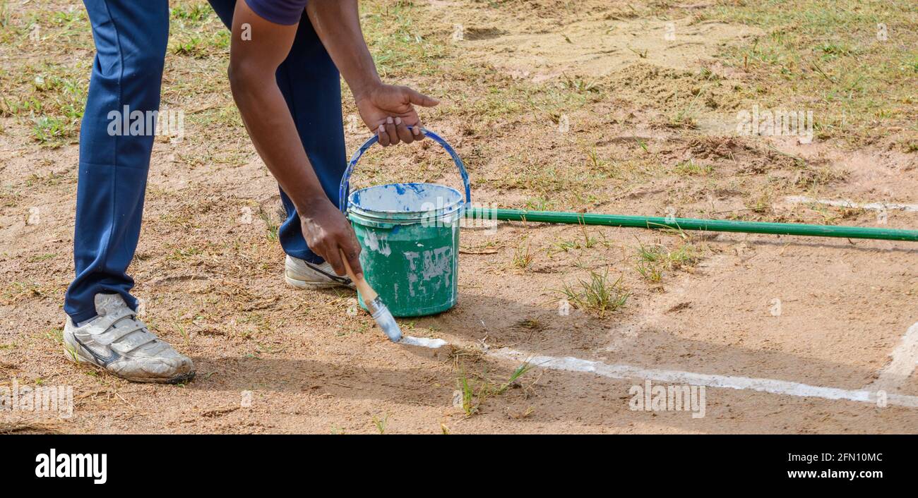 Drawing white lines in a cricket pitch, male hands with a brush and white paint, painting straight lines on the ground. preparation for the softball c Stock Photo