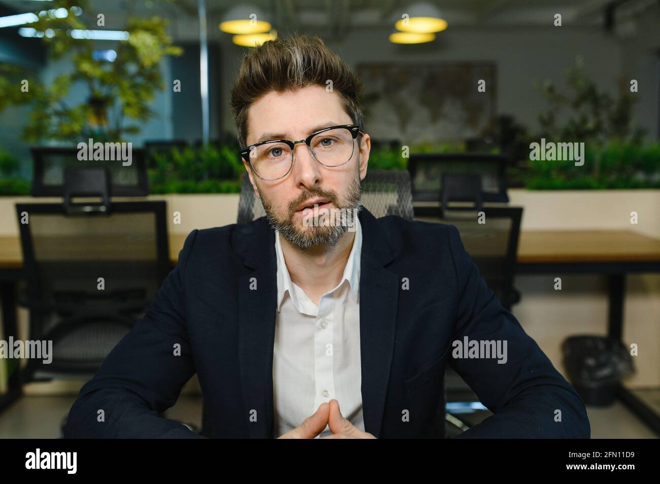 Head shot portrait confident businessman coach looking at camera and talking, mentor speaker holding online lesson, in modern office Stock Photo