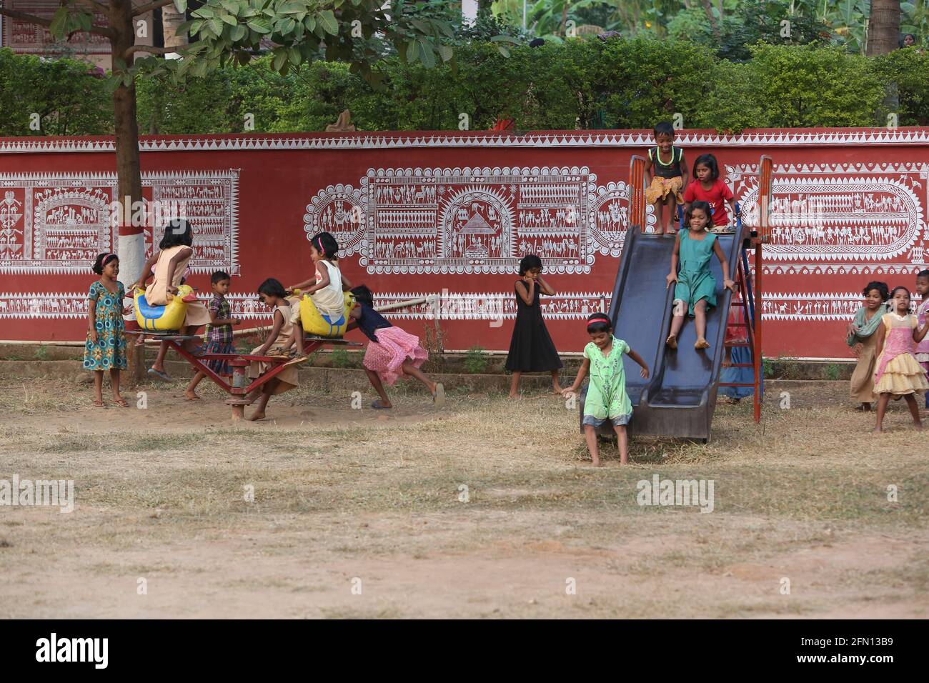 Primary school girls playing on ladder and see saw at school grounds. Traditional Saora wall painting also seen in the picture.  LANJIA SAORA TRIBE. K Stock Photo