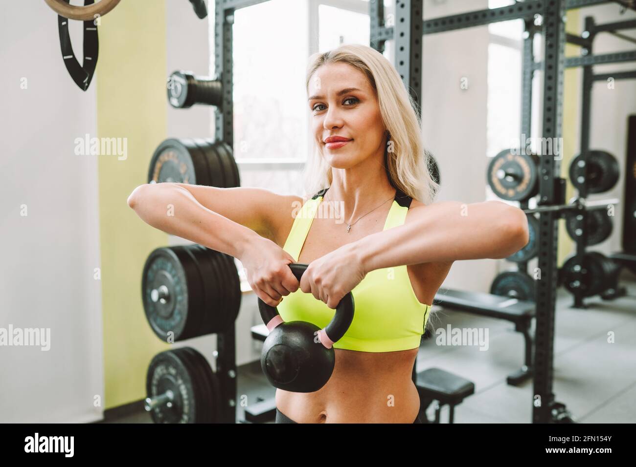 Blonde attractive woman wearing sport bra do exercises with dumbbells in fitness center or gym