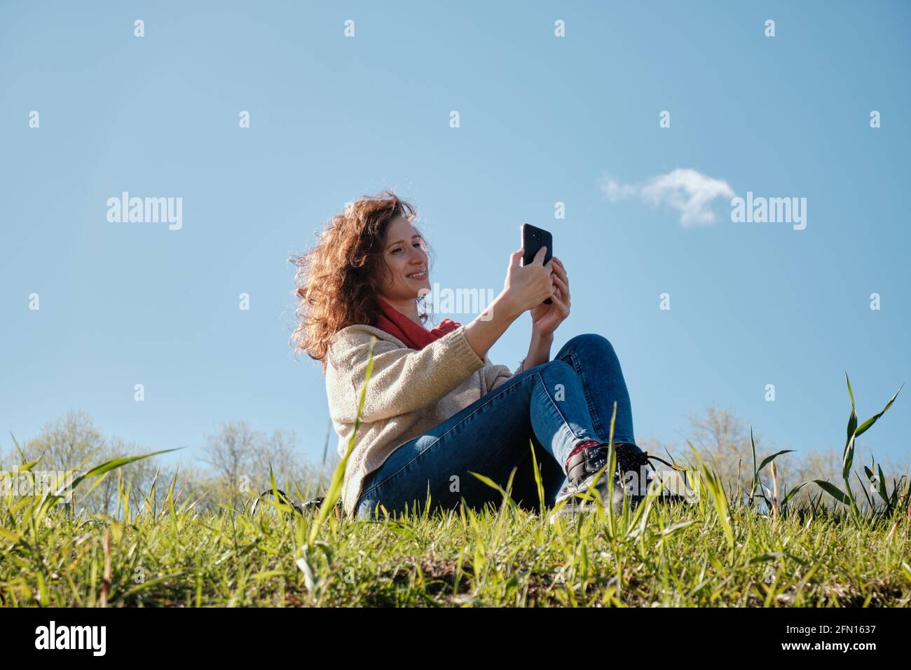Young girl with a phone in her hands, green grass and blue sky Stock Photo
