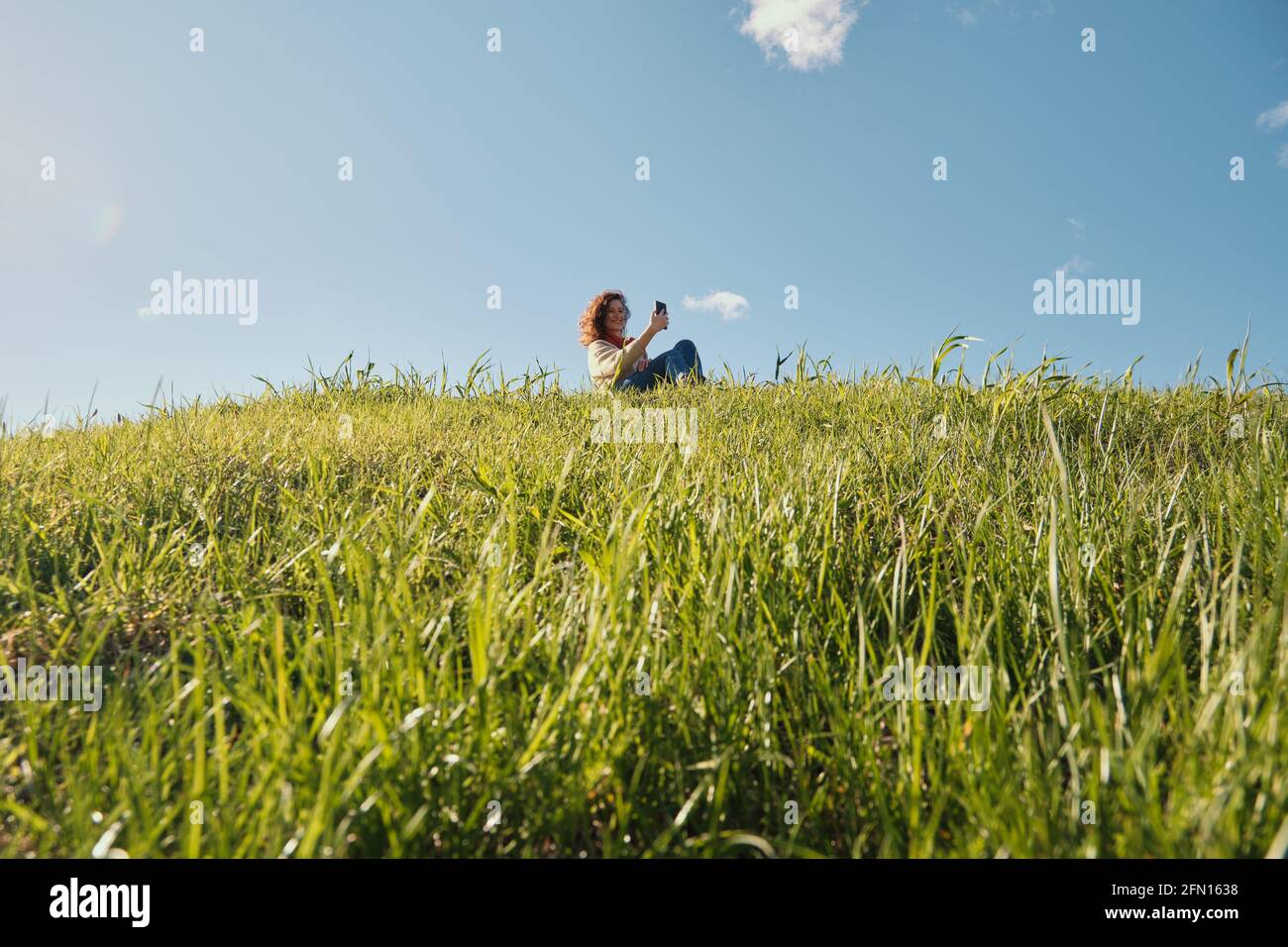 Young girl with a phone in her hands, green grass and blue sky Stock Photo