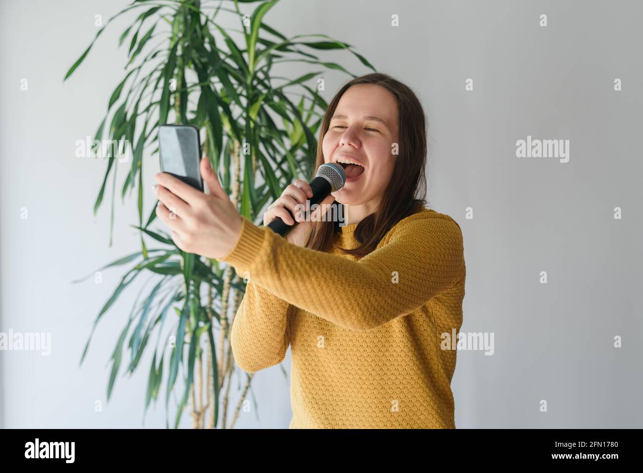 Woman blogger singing with microphone at home with expression. Taking selfie or video stream Stock Photo
