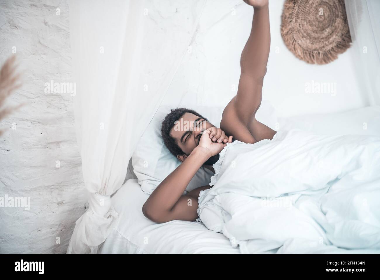 Darkskinned yawning man lying in white bed Stock Photo