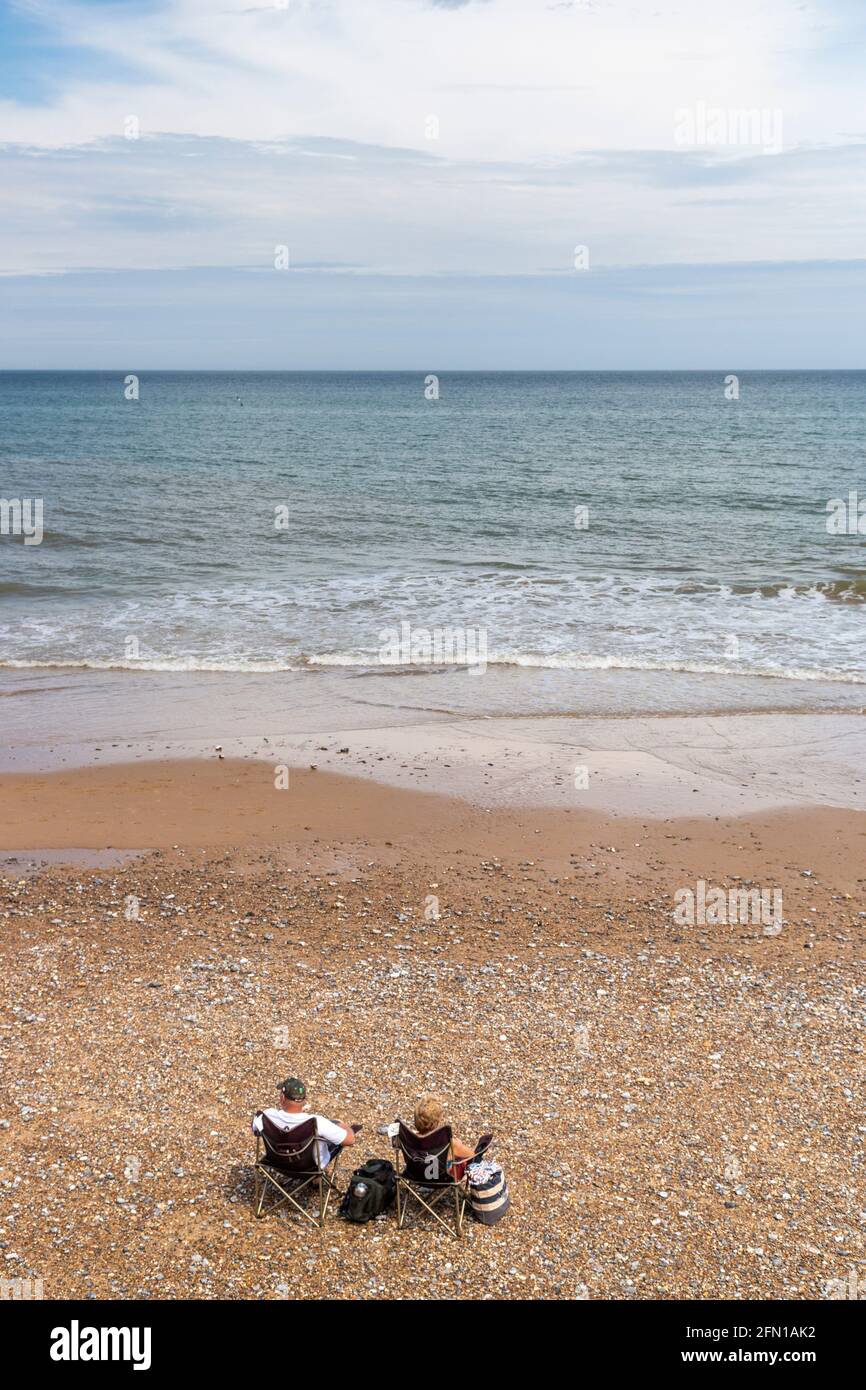 Isolated couple (in COVID-19 times) seated in loneliness on Overstrand Beach, Norfolk, UK Stock Photo