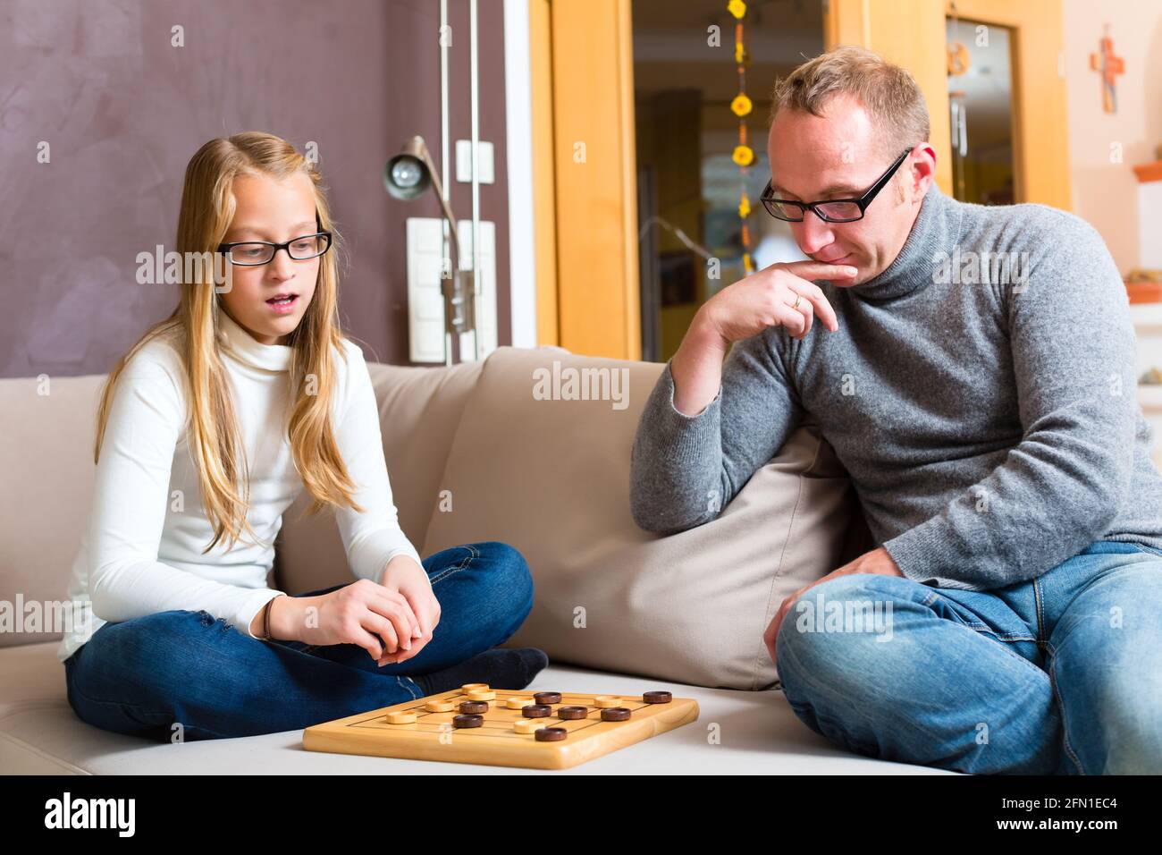 Father and daughter playing parlor or board game checkers on sofa Stock Photo