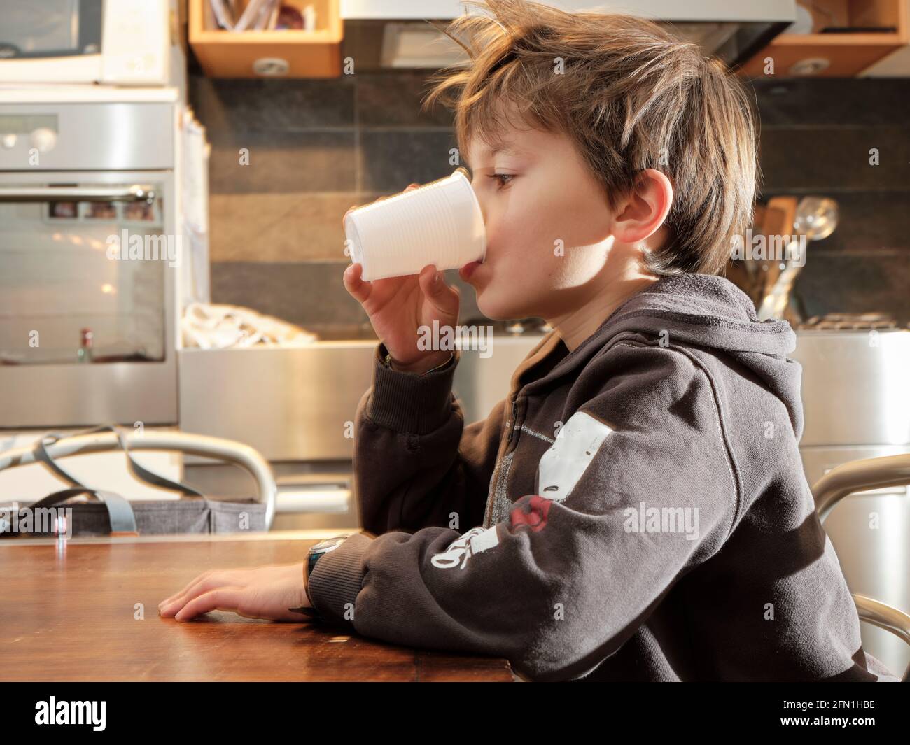 The child drinks fresh water from a white plastic cup in the home ...