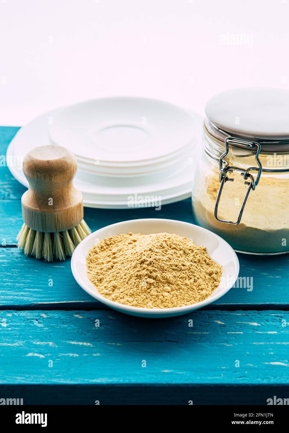 Using mustard powder for washing the dishes concept. White clean plates with bowl of yellow mustard powder and wooden dish washing brush and class jar Stock Photo