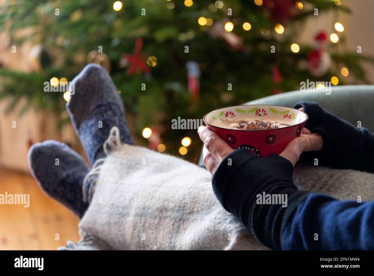 A large mug of hot chocolate being held in front of a Christmas tree - feeling cosy. Stock Photo