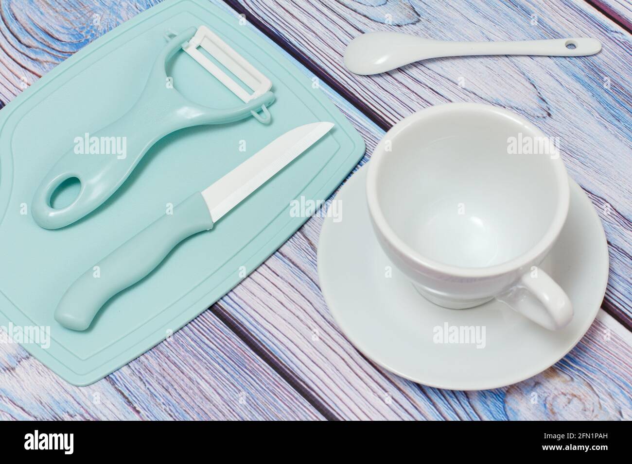 Porcelain cup with a saucer and a cutlery set on wooden boards. Top view. Kitchen ceramic knife, a scrubber on a cutting board and a spoon. Top view. Stock Photo