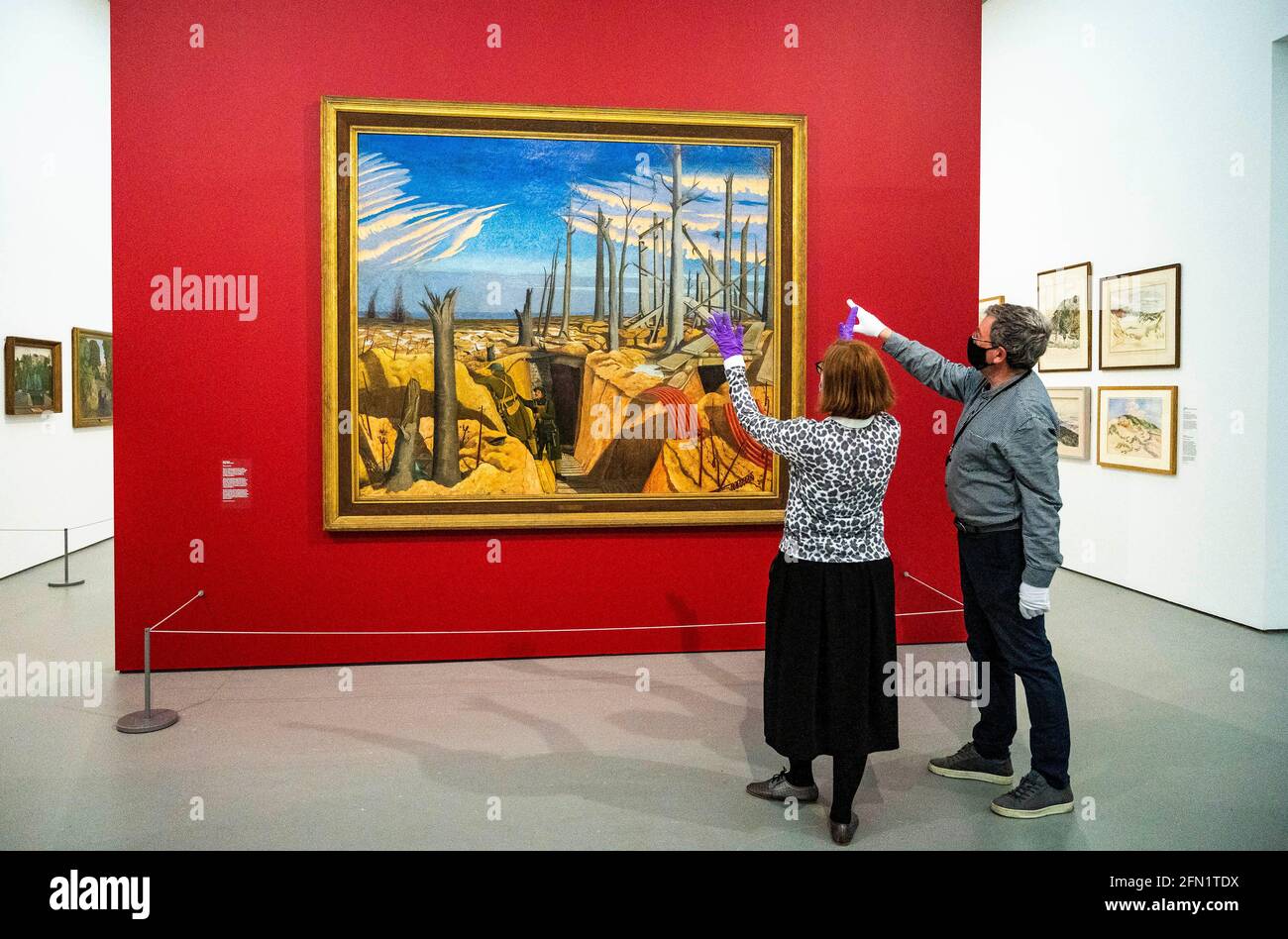 Brighton UK 13th May 2021 - Co-curators Sara Cooper and Andy Friend with the famous Oppy Wood painting (on loan from the Imperial War Museum ) by John Nash at the Towner Eastbourne as they prepare to present the first major exhibition of John Nash works in 50 years, as galleries across England reopen after lockdown. Towner Eastbourne presents the most comprehensive exhibition of work in over 50 years by John Nash, one of the most versatile and prolific artists of the 20th century. Credit: Simon Dack/Alamy Live News Stock Photo