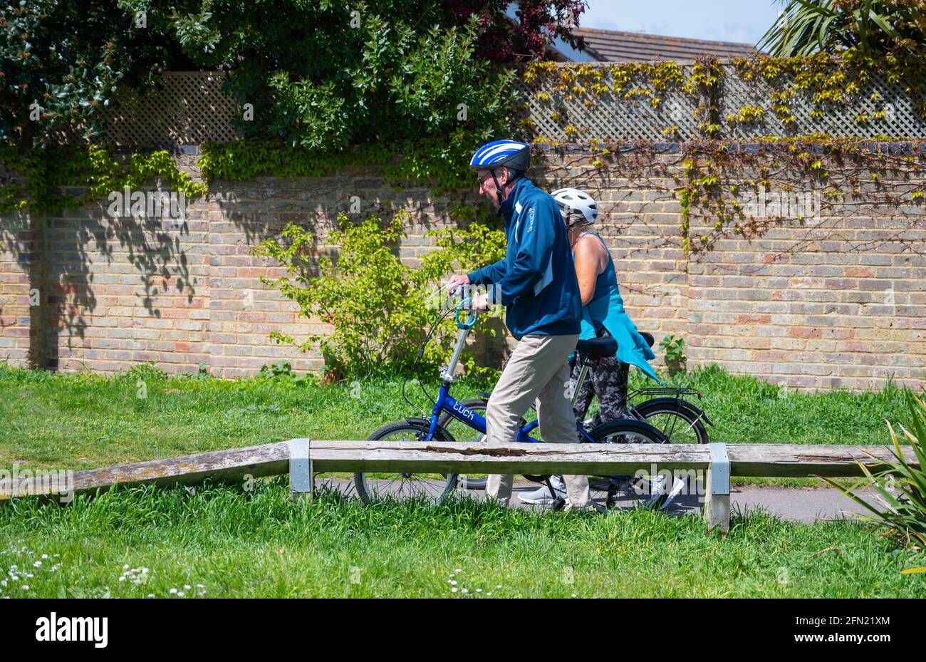 Pair of middle aged people, male and female, pushing bicycles through a park in the UK. Stock Photo