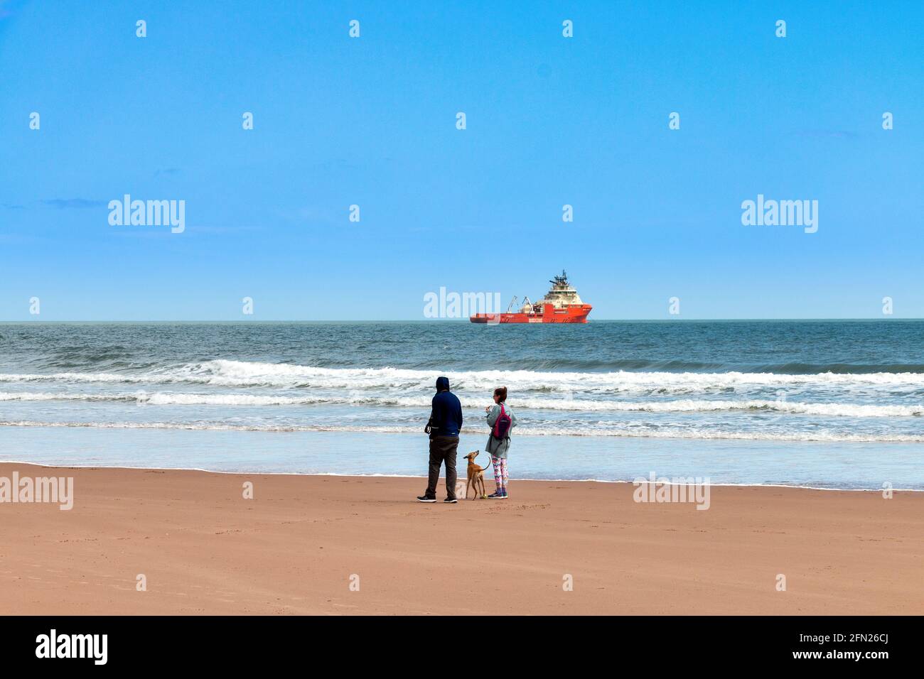 LUNAN BAY AND BEACH ANGUS SCOTLAND PEOPLE ON THE SANDY BEACH AND THE SEA WITH OIL RIG SUPPORT VESSEL Stock Photo