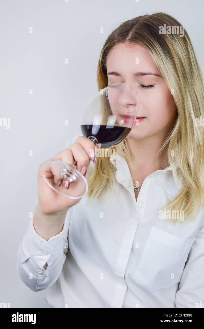 Portrait of a beautiful young blond woman sniffing red wine in the glass to feel its bouquet at a wine tasting Stock Photo