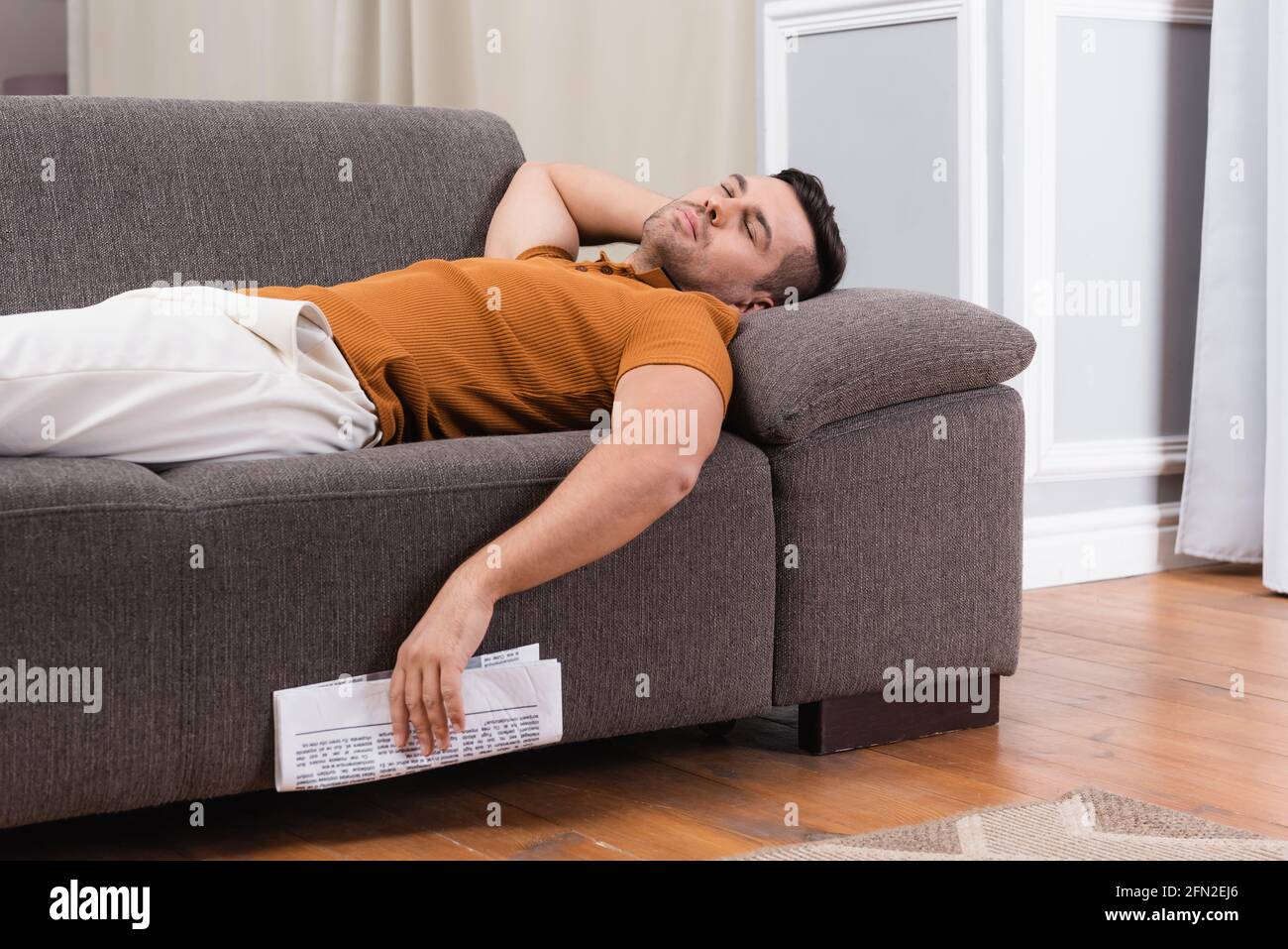 young man sleeping on couch while holding newspaper Stock Photo