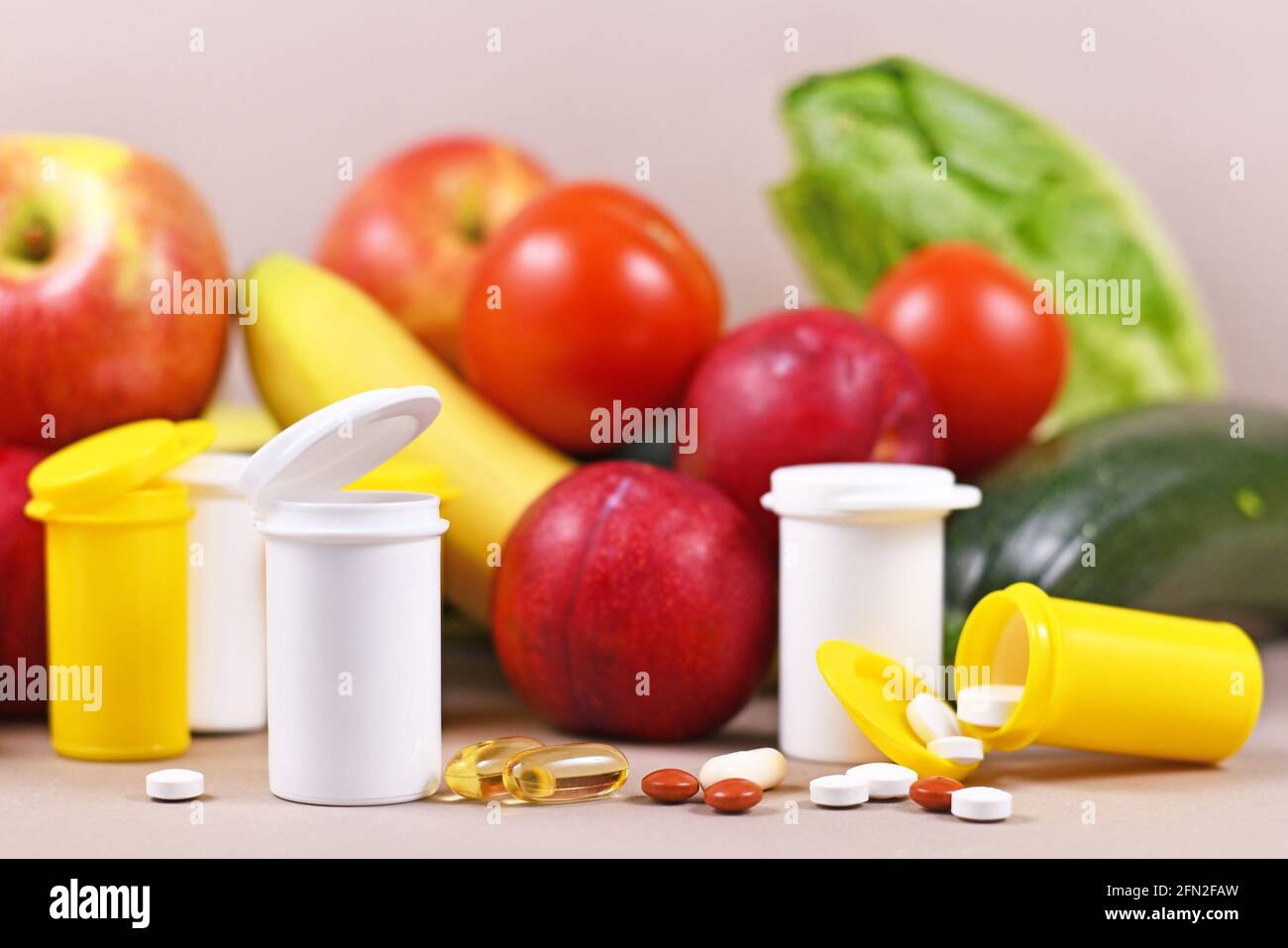 Pills of food nutrition supplements in front of fruits and vegetables in background Stock Photo