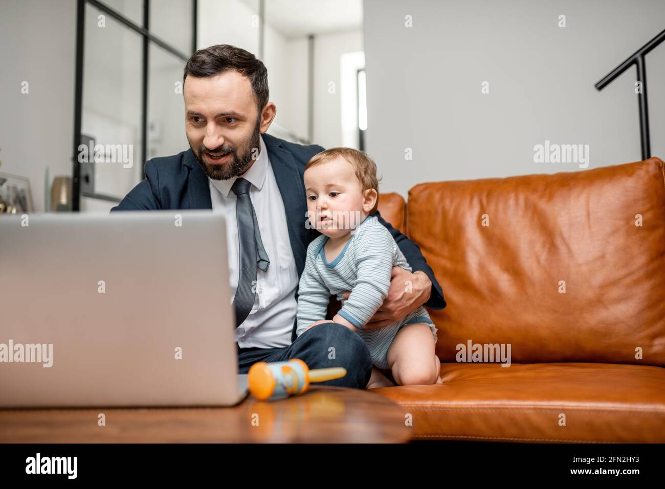 Young businessman dad working on a laptop at home while taking care of his newborn son. Multitasking and babysitter. Stock Photo