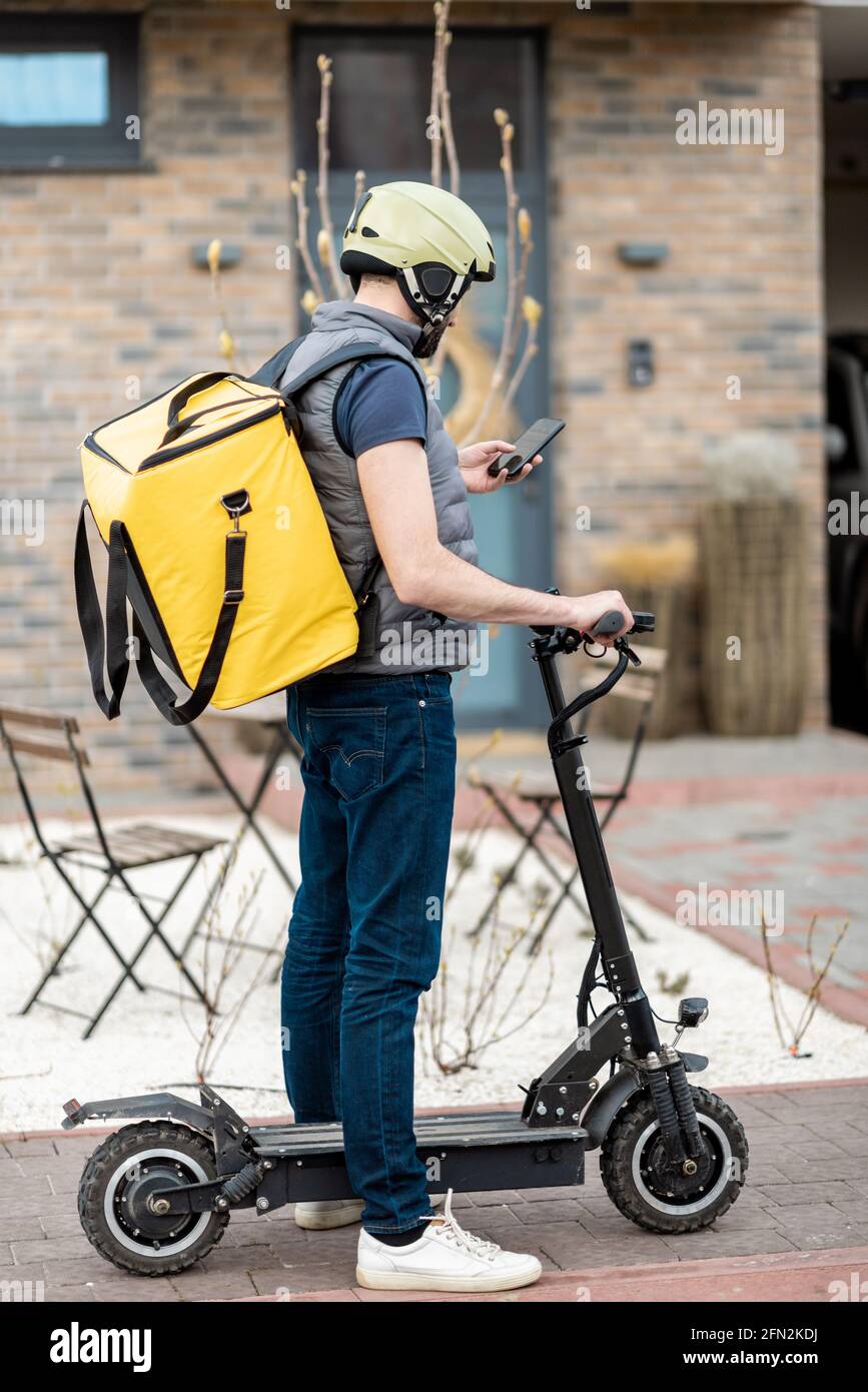 Delivery man in helmet with yellow backpack rides electro scooter on ...