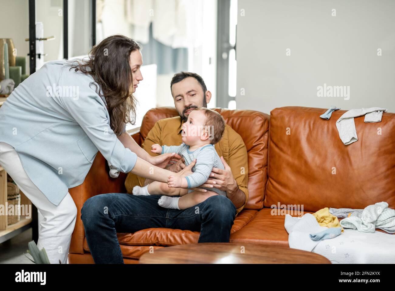 Mother takes a newborn baby nursed by dad at home, hugs and kisses. Parenthood and raising a baby concept. Stock Photo