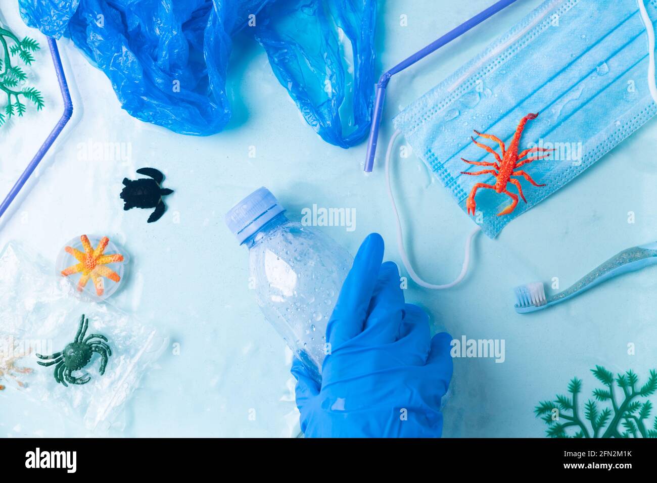 Pollution concept. Hand in blue glove takes plastic bottle from the ocean small marine fishes Stock Photo