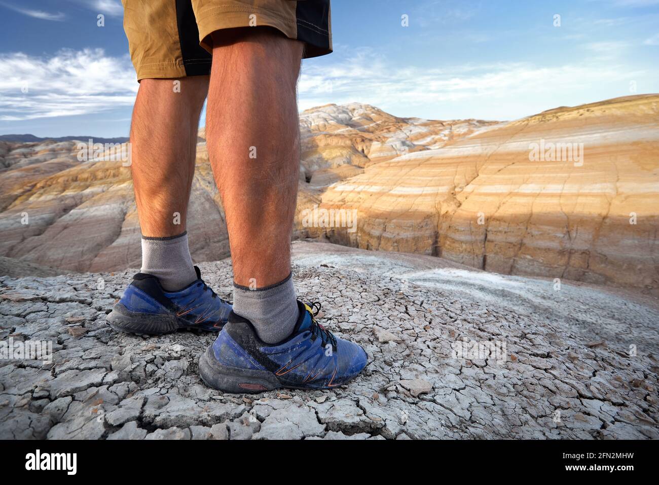 Close up of muscle legs of young runner in sport blue hoes at drought cracked earth red desert mountains in Kazakhstan Stock Photo