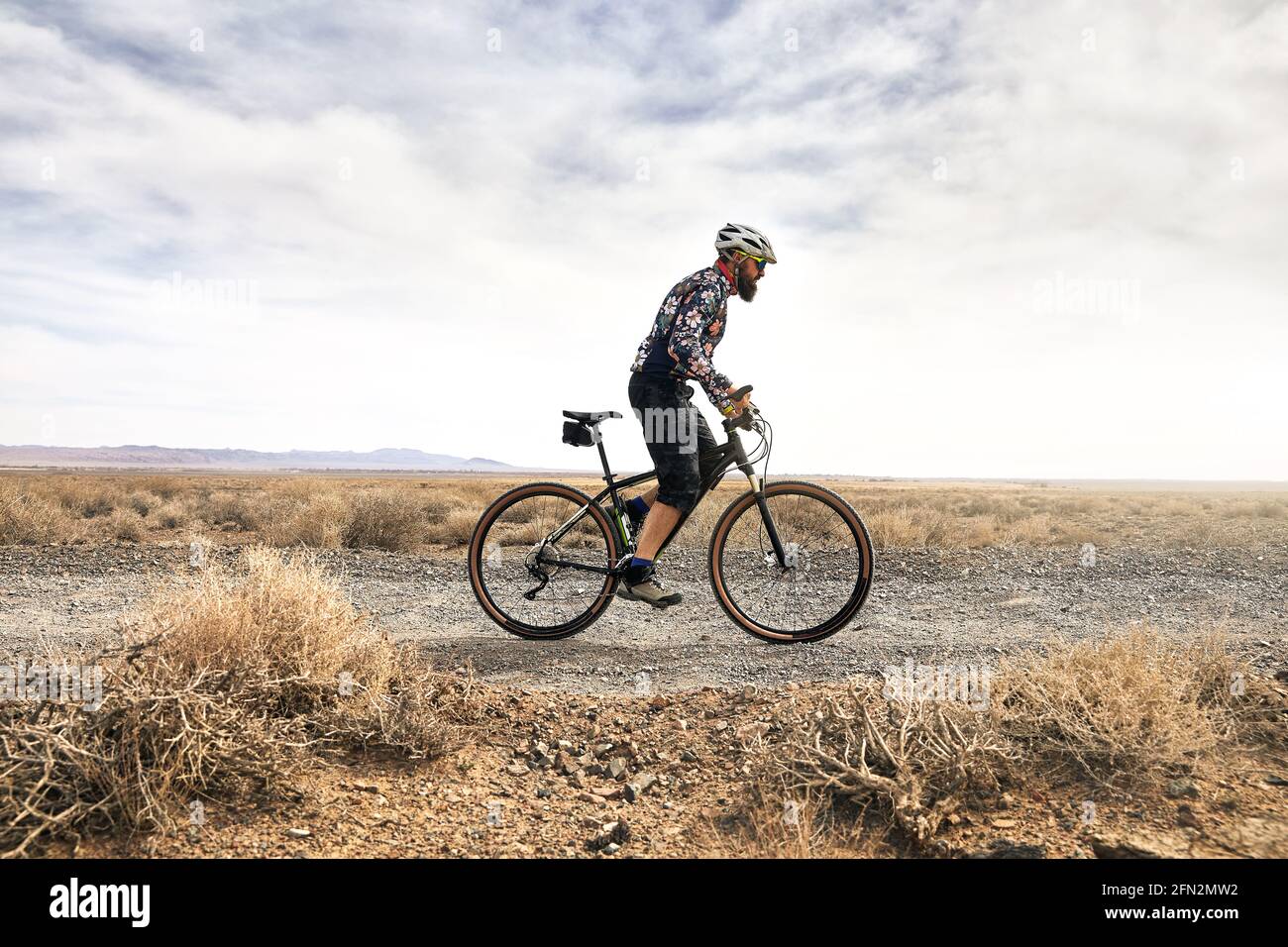 Rider with beard rides his mountain bike in the desert road at sunny weather in Kazakhstan. Extreme Sport and outdoor recreation concept. Stock Photo