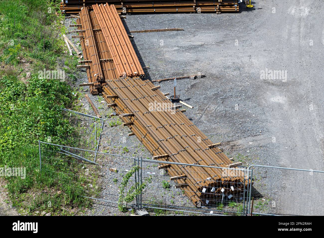 Long and thick, rust-covered steel bars stacked outside on a gravel square, viewed from above. Stock Photo