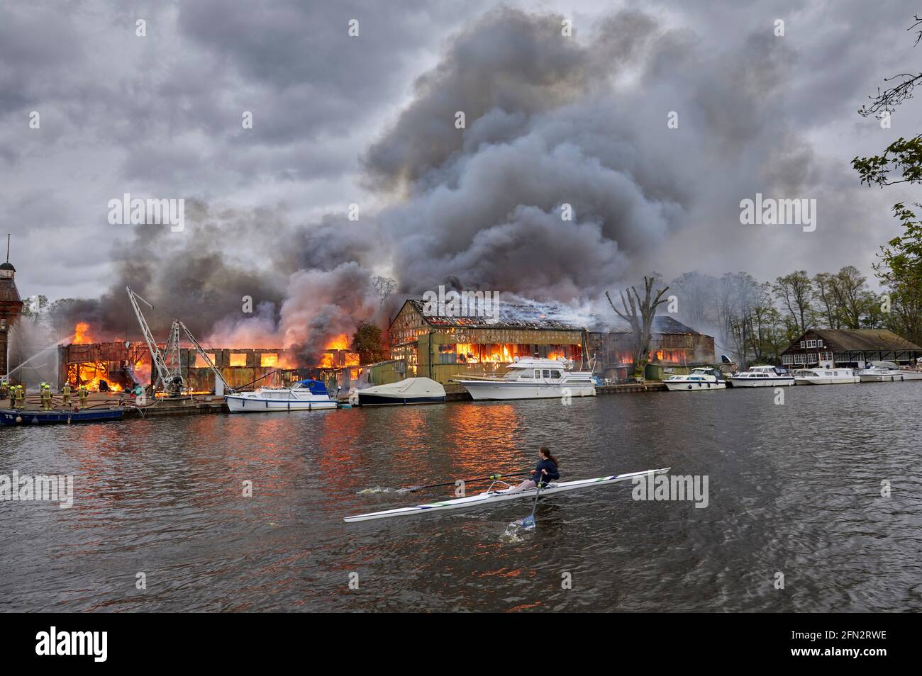 Rower from Wimbledon High School passing the Platt's Eyot fire of 3 May 2021 which destroyed the boat shed of Otter Marine and the Dunkirk evacuation Stock Photo