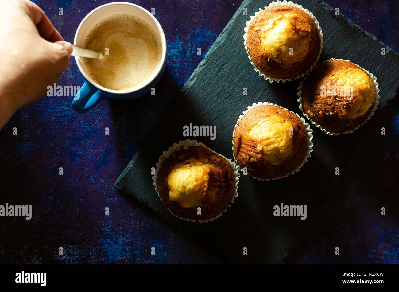 Stirring breakfast coffee with muffins on a slate plate on a rusty blue background. Dark food Stock Photo