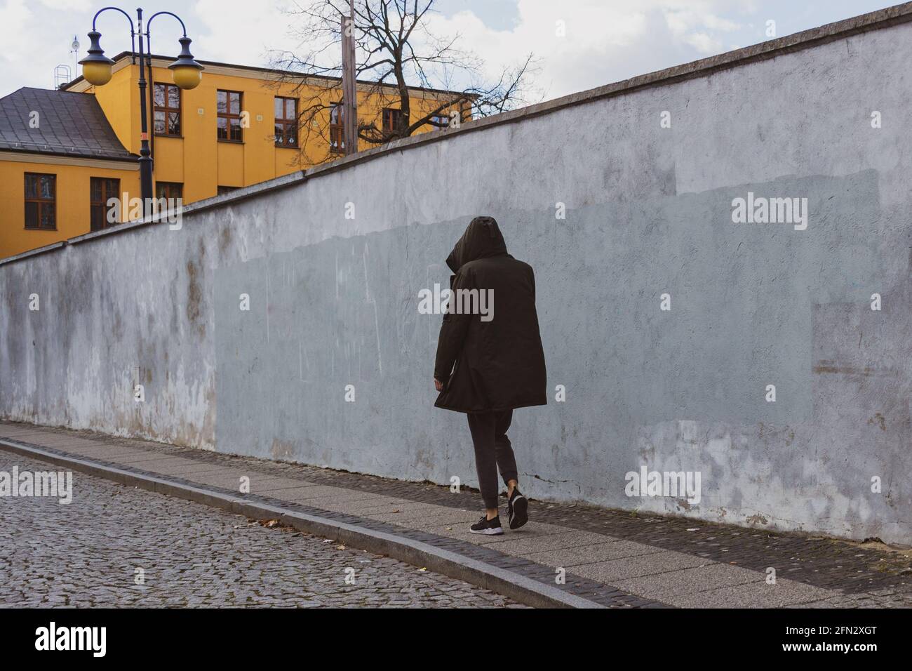 man in a hooded black jacket walking on the street Stock Photo