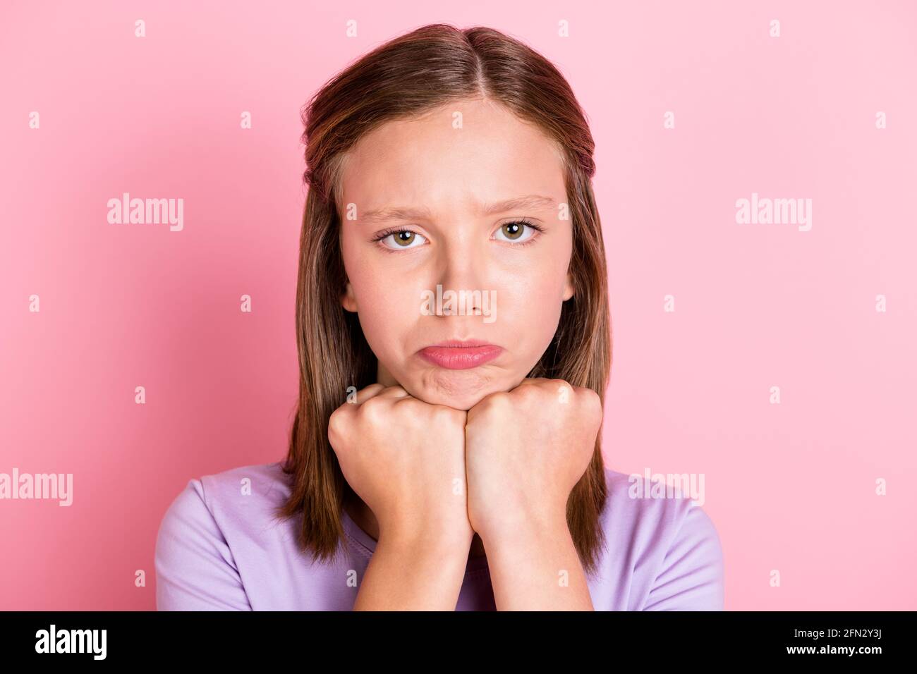 Photo of unhappy small girl bad mood hold fists chin sad face isolated on pastel pink color background Stock Photo