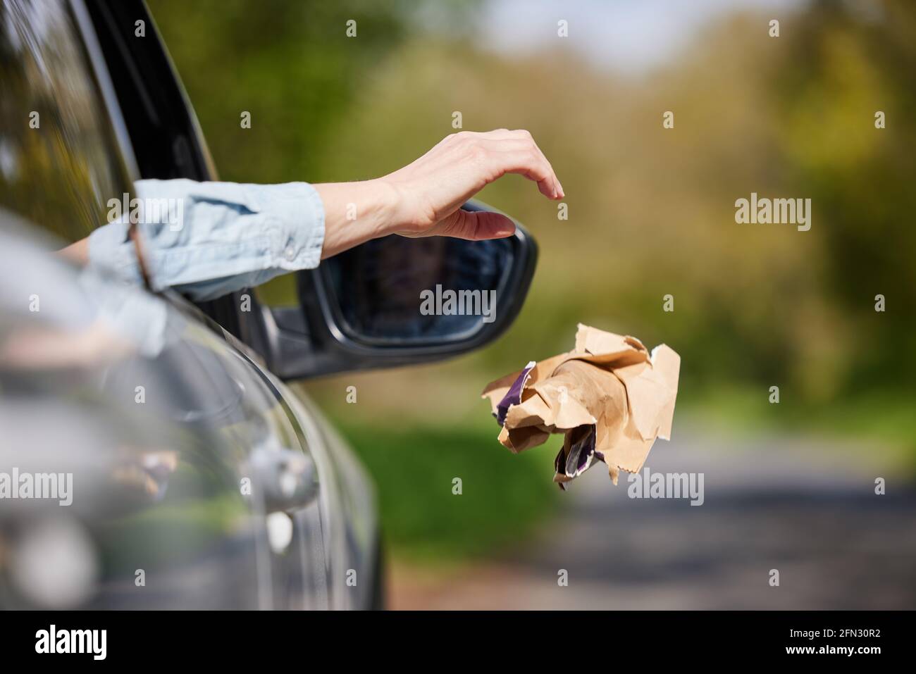 Close Up Of Driver In Car Dropping Trash Out Of Window On Country Road Stock Photo