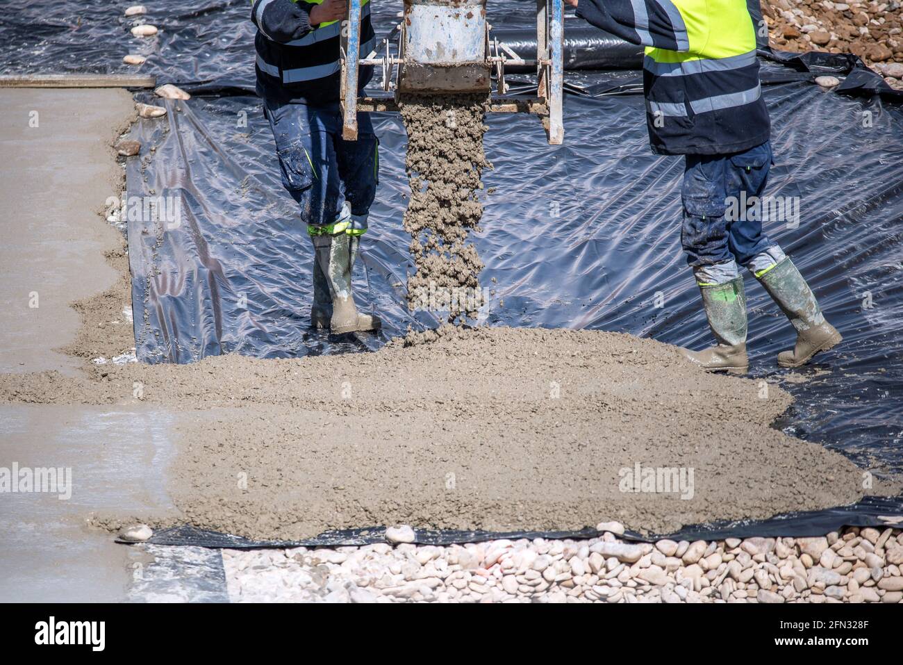 Two construction workers at work pouring a mixture on a floor with a plastic sheet. Stock Photo