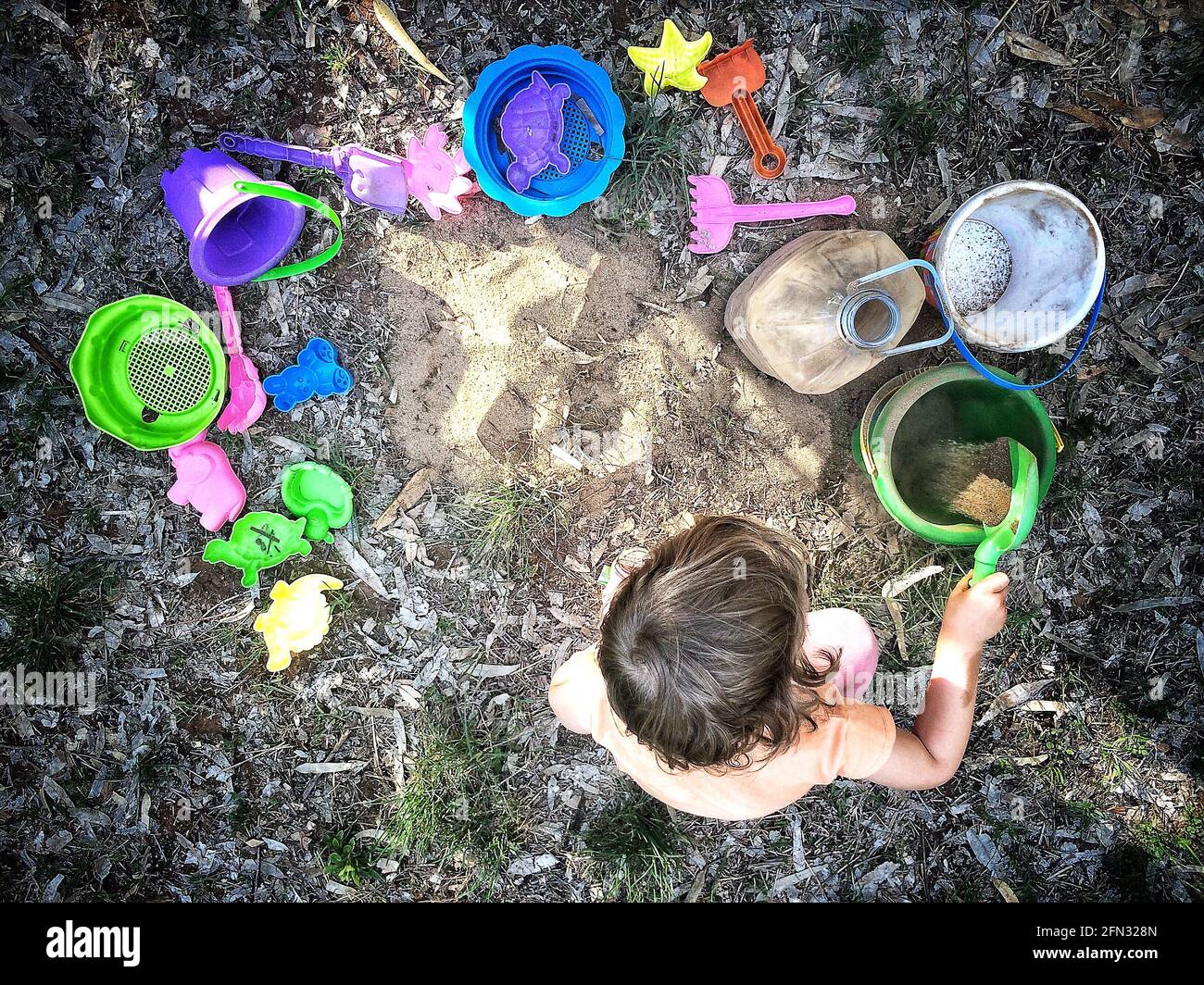 Child sitting on a forest floor playing with various colored toys and dirt. Stock Photo