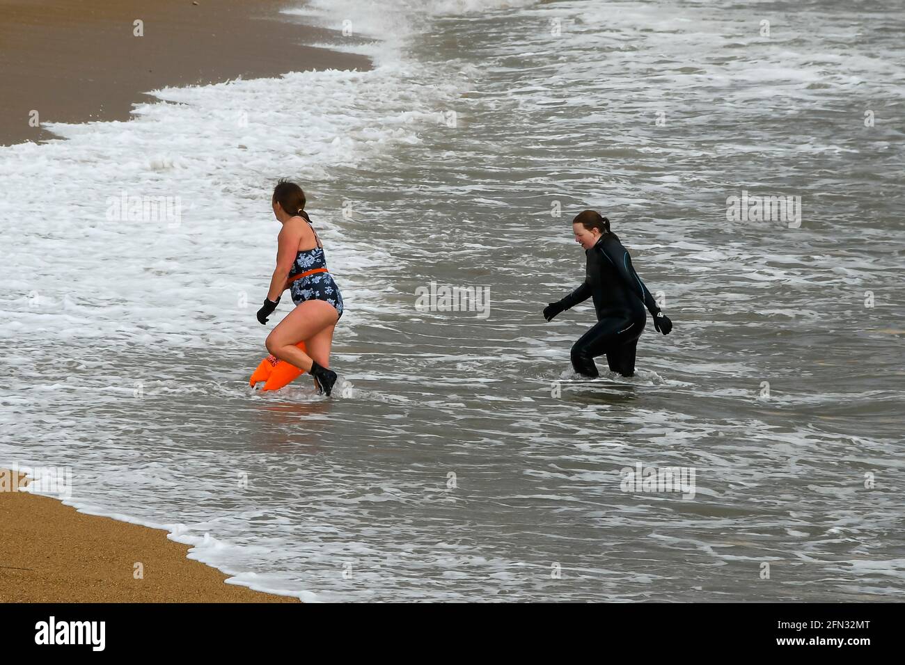 West Bay, Dorset, UK. 13th May, 2021. UK Weather. Two swimmers emerge from the sea on to the beach at the seaside resort of West Bay in Dorset on an afternoon of sunny spells and heavy showers. Picture Credit: Graham Hunt/Alamy Live News Stock Photo