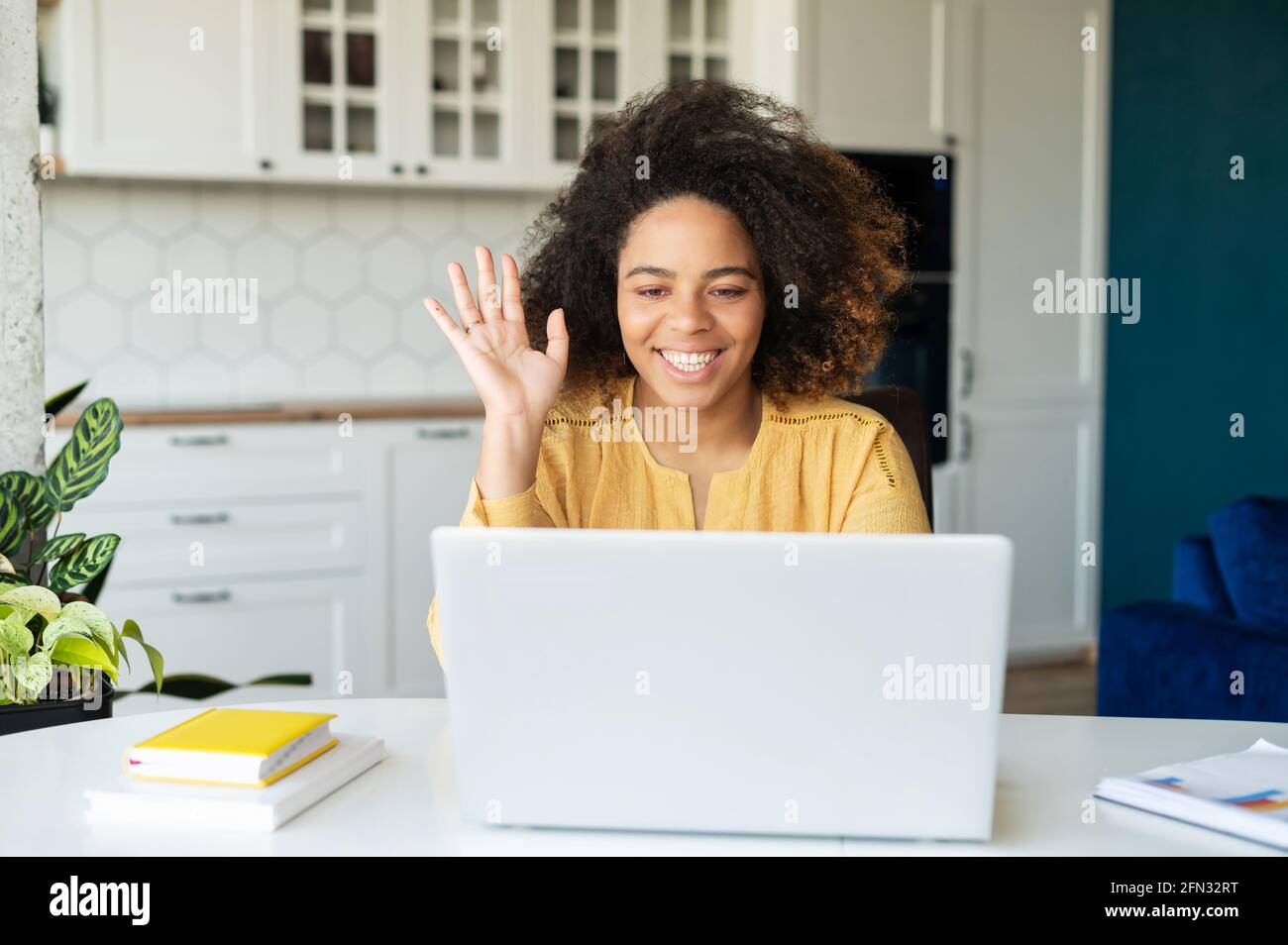 Cheerful African-American young woman involved video meeting, using laptop for online communication, waving hand, female student takes a part in online courses. Telecommuting, tutoring online Stock Photo