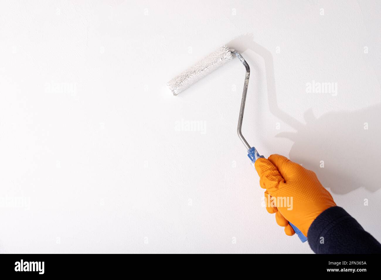 Hand in protective glove painting a wall with roller and white paint