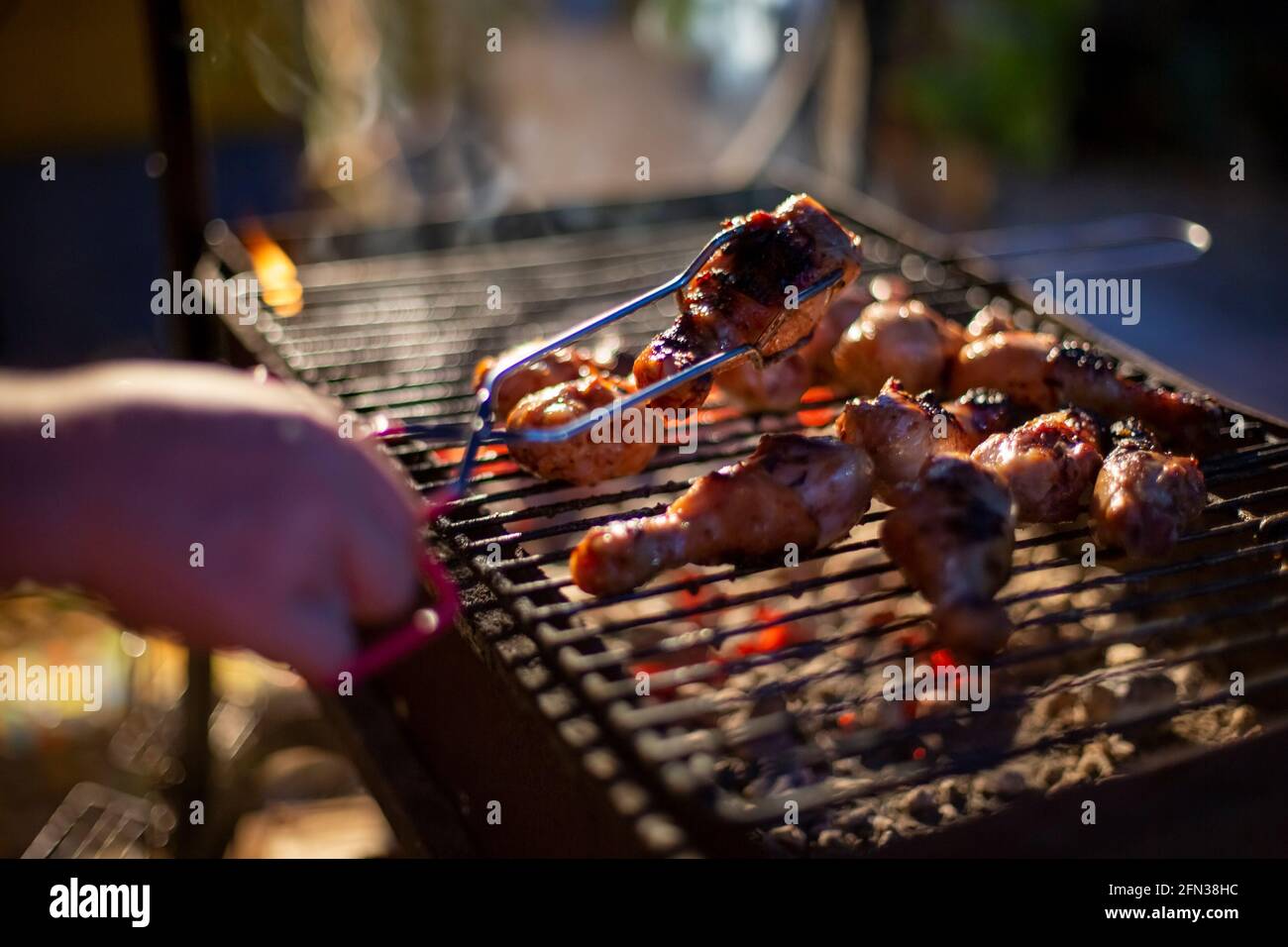 human hand turns chicken drumsticks on a barbecue grill with grilling