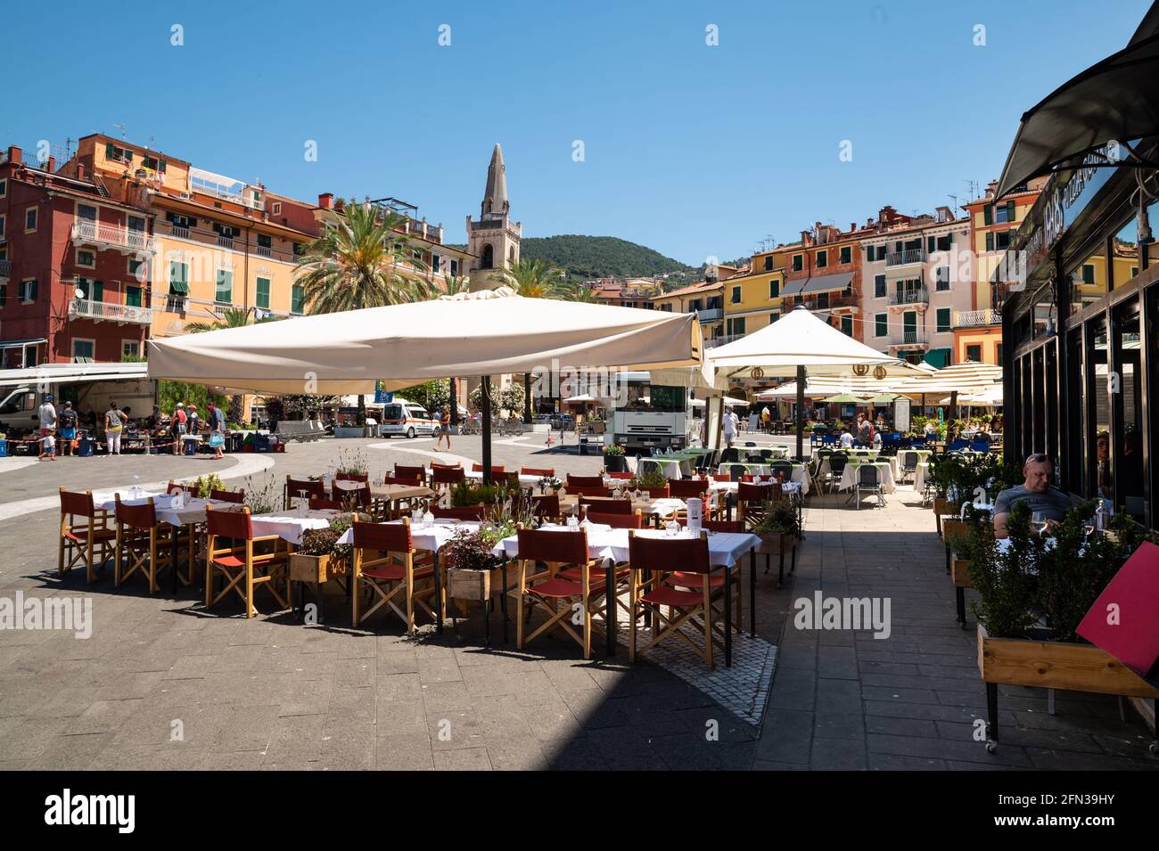 Lerici, Liguria, Italy. June 2021. The colorful houses and the bell tower overlook the square of the seaside village. The restaurants have umbrellas a Stock Photo