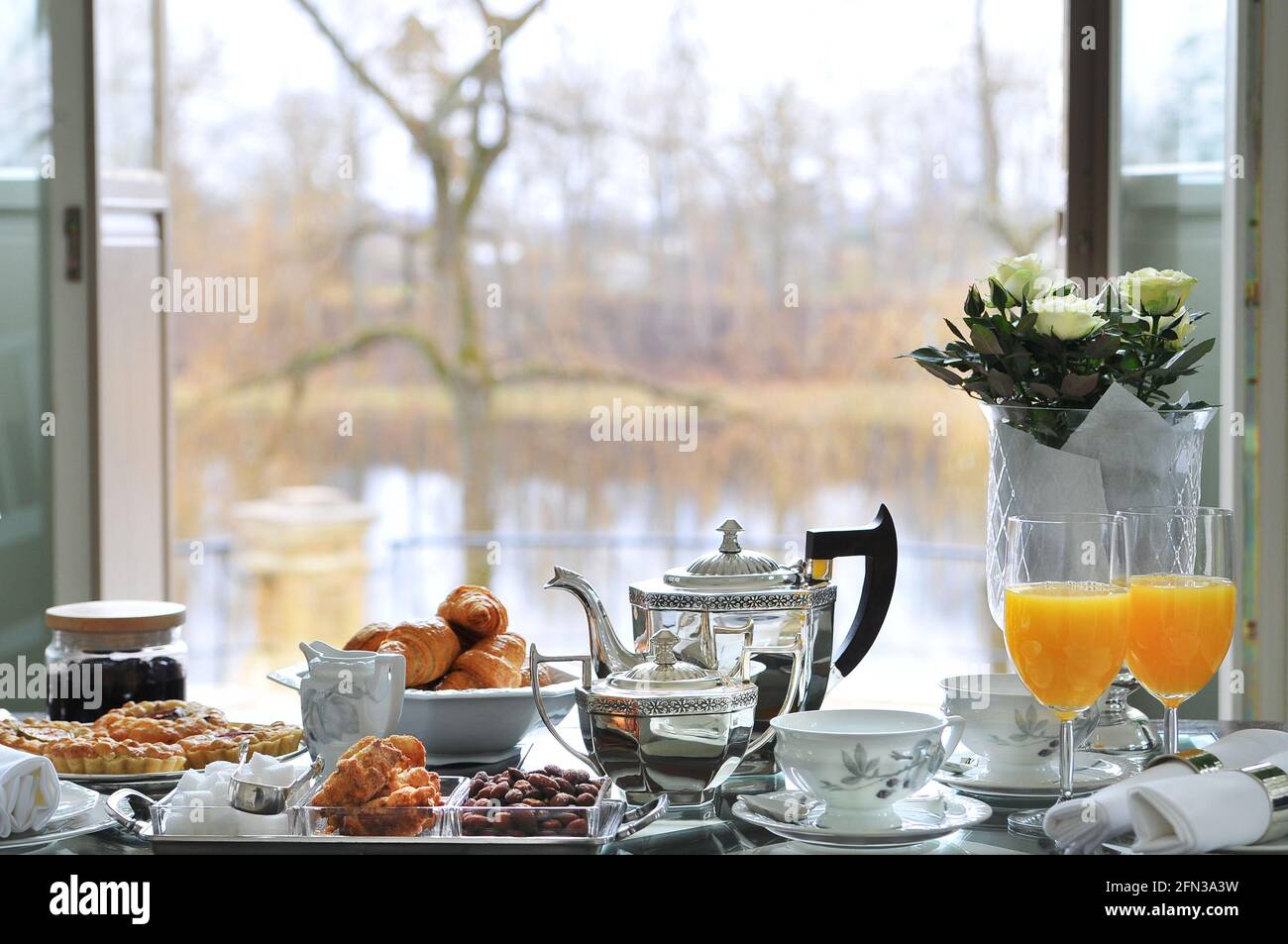 Rich breakfast serving on table with croissants, almonds, orrange juice and other pastry silverware autumn morning light Stock Photo