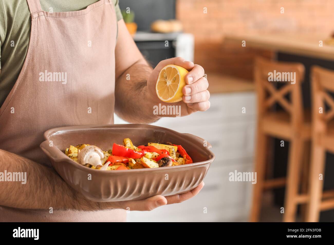 Young man squeezing lemon onto baking dish in kitchen Stock Photo
