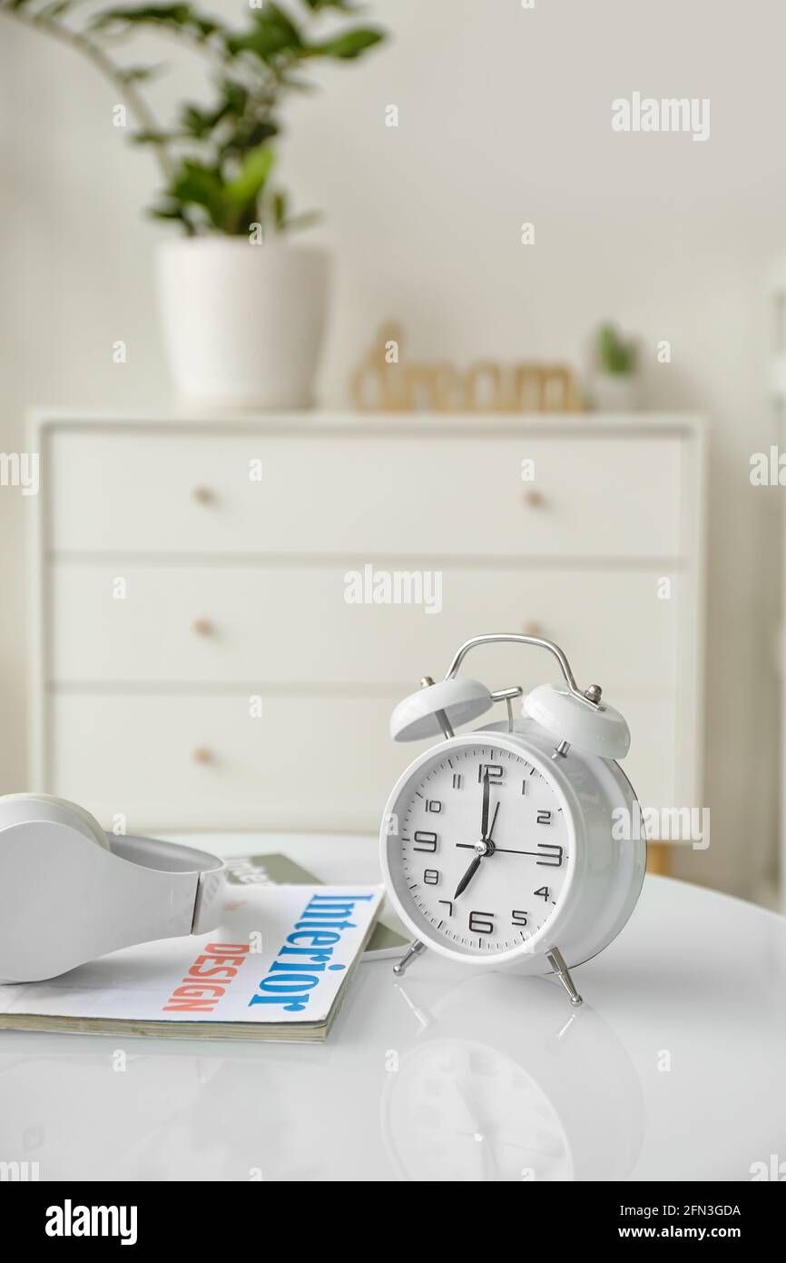 Alarm clock with headphones and magazine on table in room Stock Photo