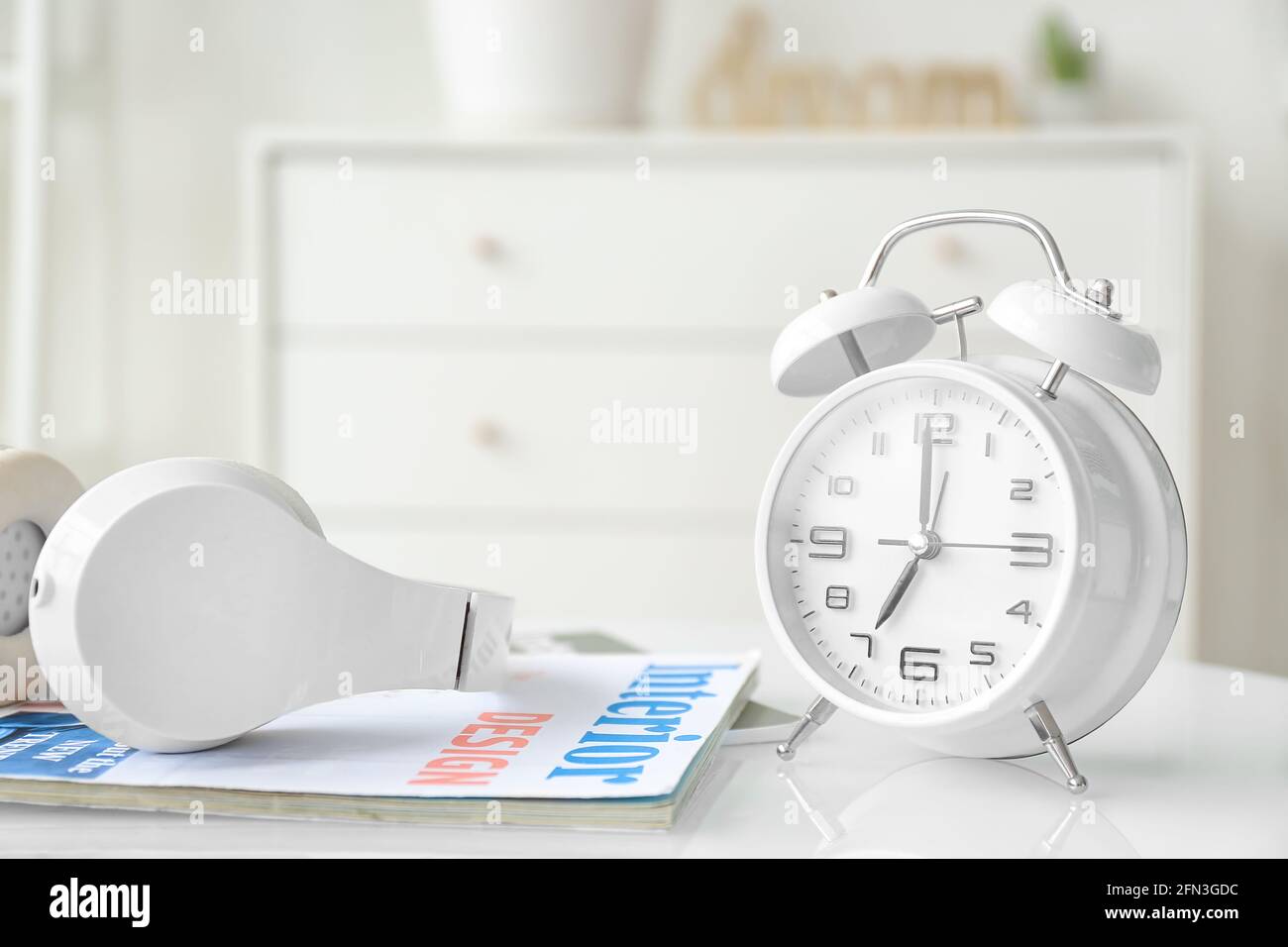 Alarm clock with headphones and magazine on table in room Stock Photo