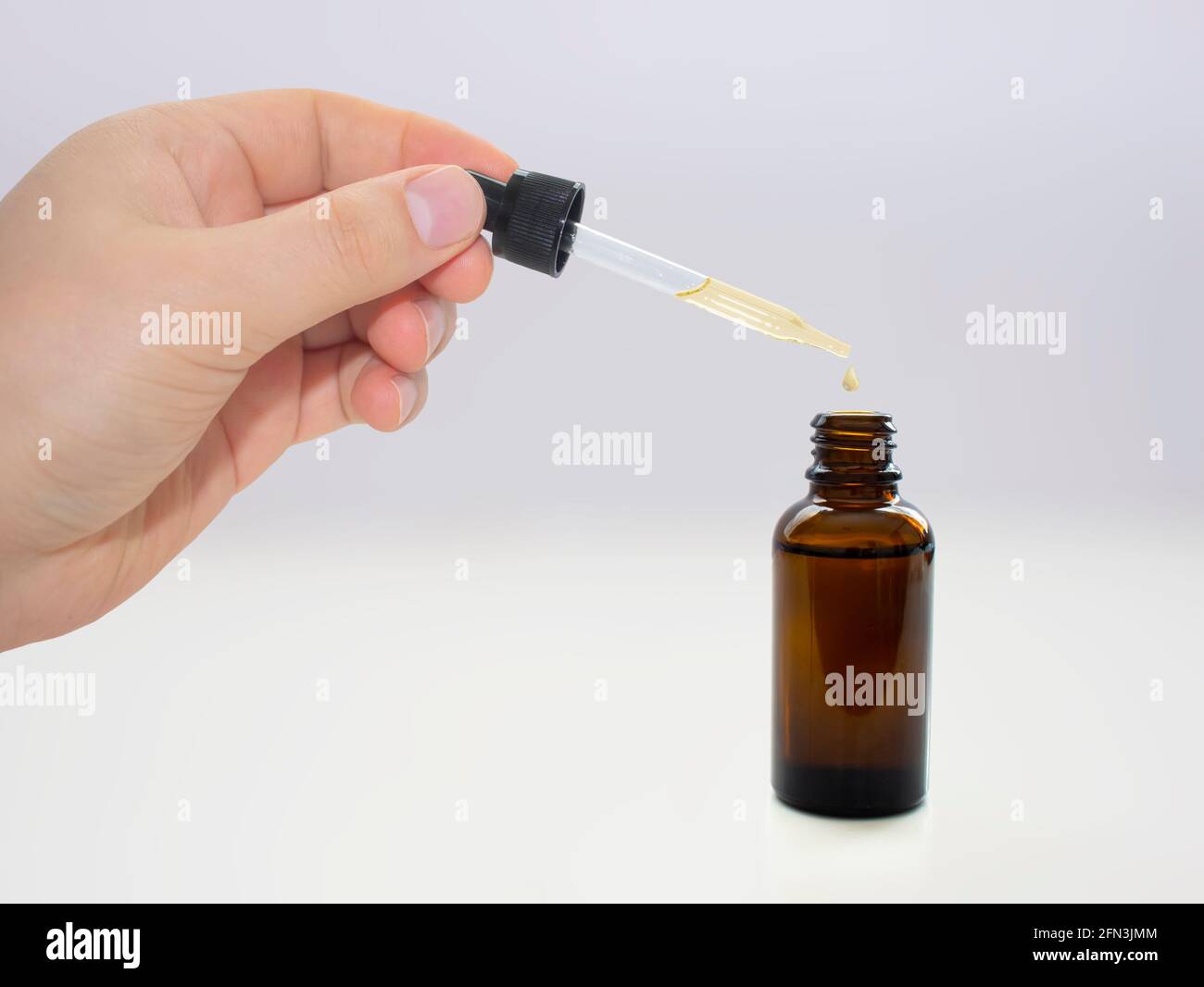 A person dropping cannabis oil on an amber bottle on clear background. Stock Photo